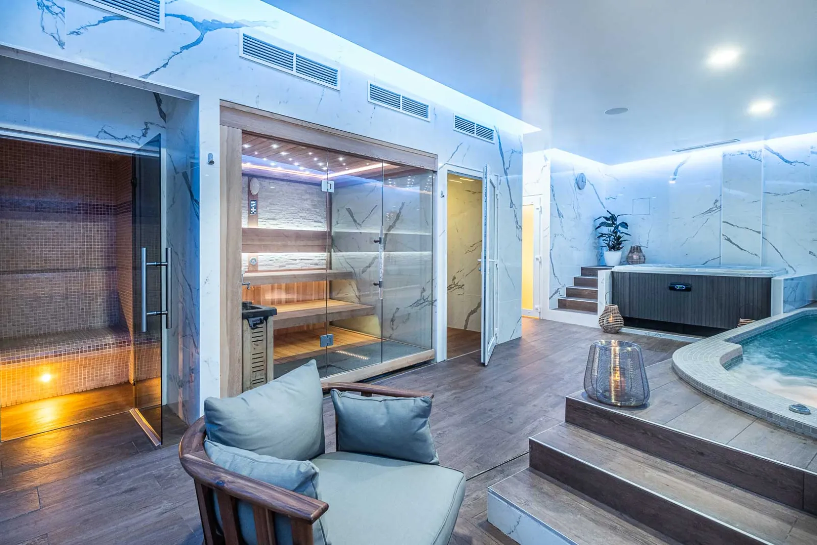 Modern luxury spa and wellness area featuring a sauna with glass doors, hot tub, relaxation seating, marble walls, and ambient lighting at Palais Gallien Hotel & Spa in Bordeaux