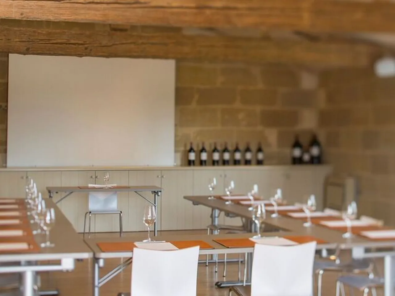 Modern conference room with wooden tables, white chairs, water glasses, and a blank whiteboard on the brick wall at Château Haut-Bailly in Bordeaux