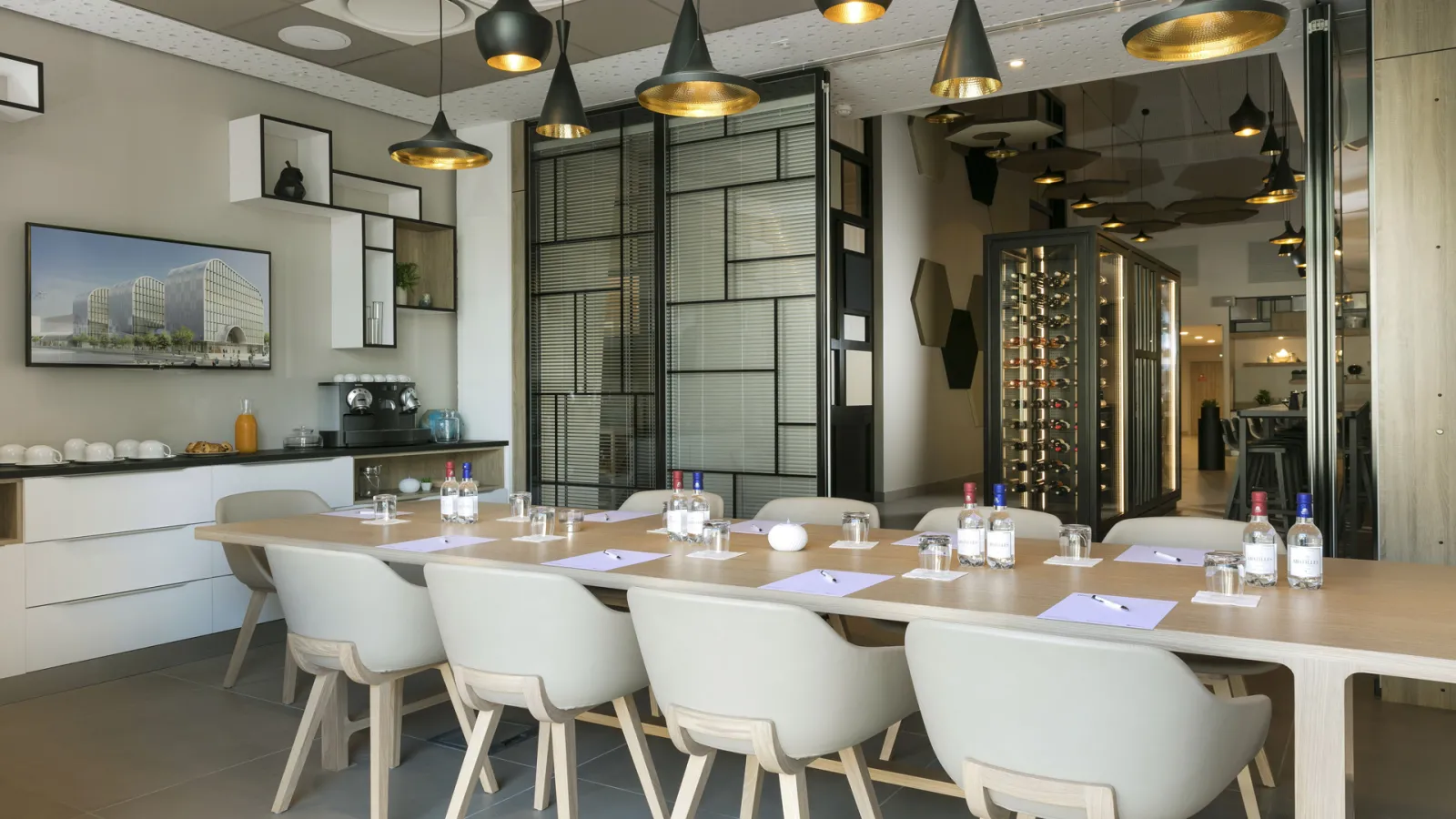 Modern conference room at Hilton Garden Inn Bordeaux Centre with a long wooden table, white chairs, pendant lighting, glass partitions, and refreshments setup