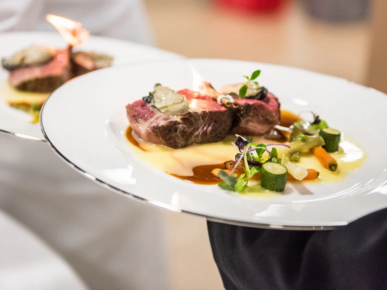 Fine dining plate featuring a seared duck breast fillet served on a creamy sauce, garnished with seasonal vegetables and microgreens, presented on a white plate