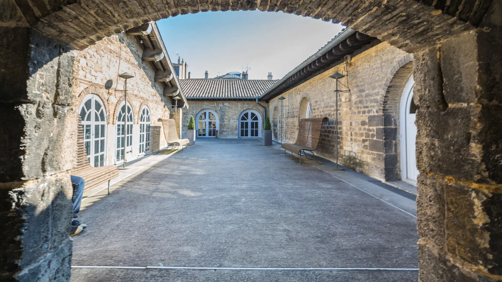 Interior courtyard of the CAPC Museum of contemporary art in Bordeaux, featuring restored stone arches, Gothic-style windows with white frames, and a modern roof structure against a clear blue sky.