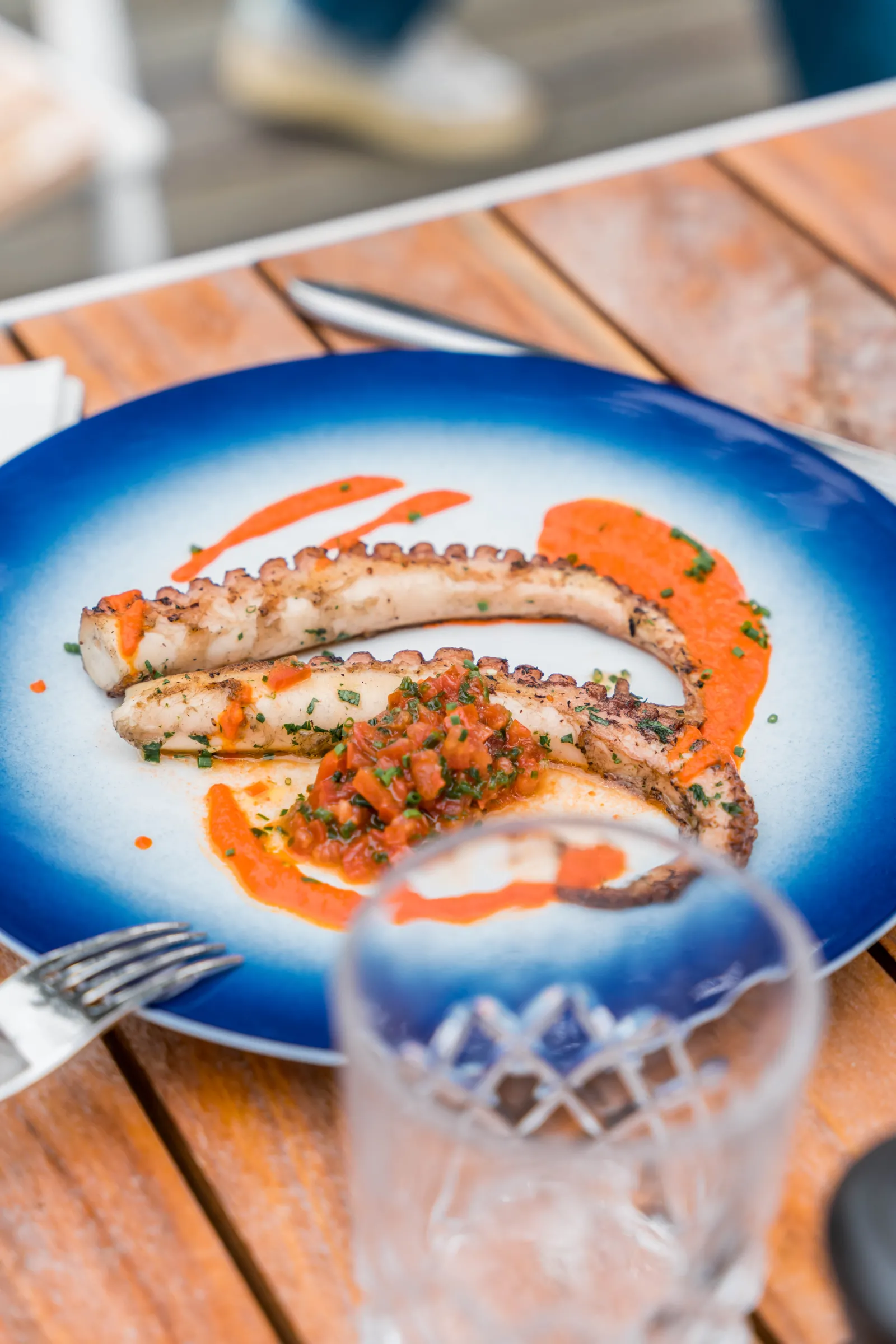 Grilled octopus tentacles served on a blue plate with orange pepper garnish and fresh herbs, presented at a restaurant in Bordeaux