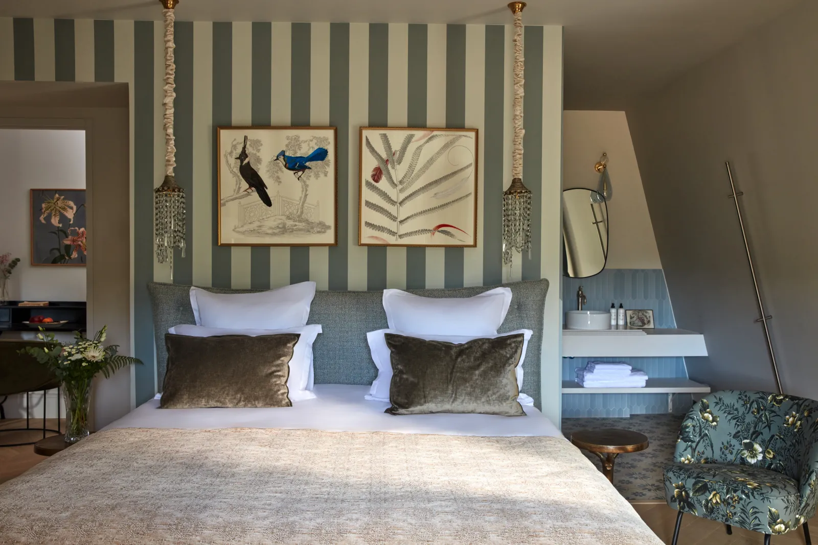 Elegant bedroom with striped wallpaper, upholstered headboard, botanical artwork, hanging planters, and modern furnishings at Château Léognan in Bordeaux