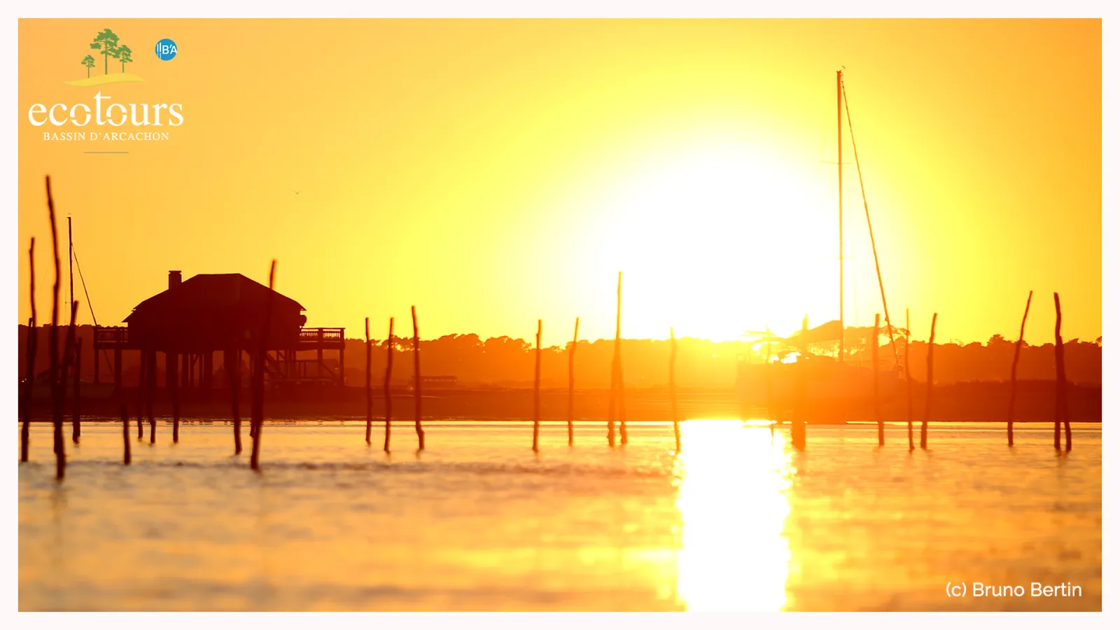 Sunset over the Arcachon Basin with traditional wooden stilt houses and sailboats silhouetted against golden light reflecting on the water