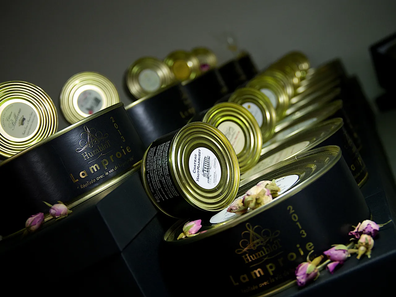 Collection of luxury candles with gold-rimmed lids and black labels decorated with purple flowers, arranged in a diagonal display