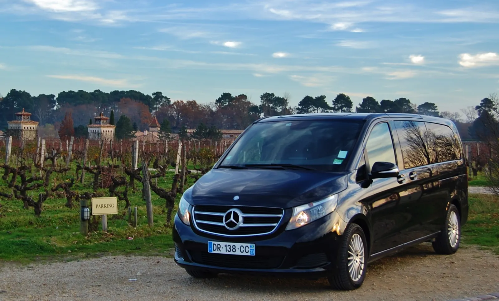 Black Mercedes minivan parked in a vineyard near Bordeaux with historic château towers in the background and rows of grapevines