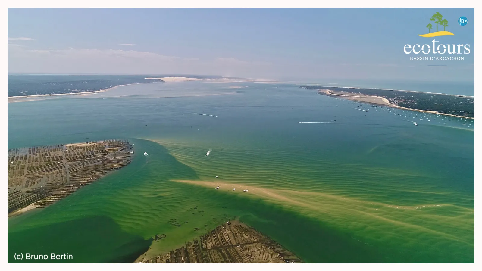 Aerial view of Arcachon Basin showing turquoise waters, wooden oyster farming structures, sandy banks, and surrounding coastal landscape with boats scattered throughout the bay.