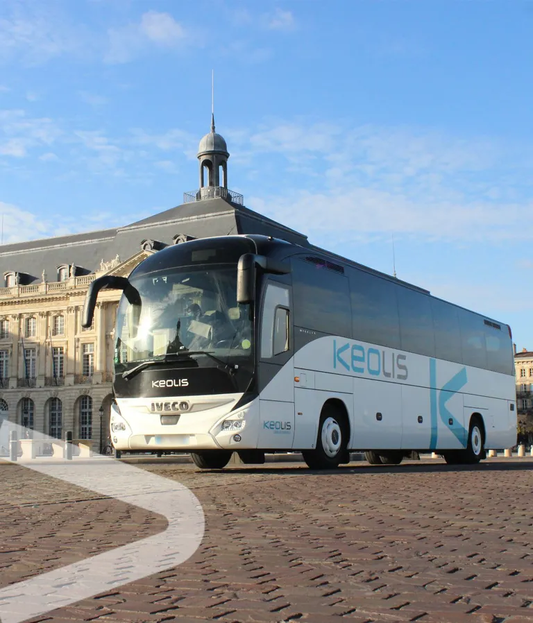 A white and blue Keolis coach bus parked in front of a classical building with a dome in Bordeaux
