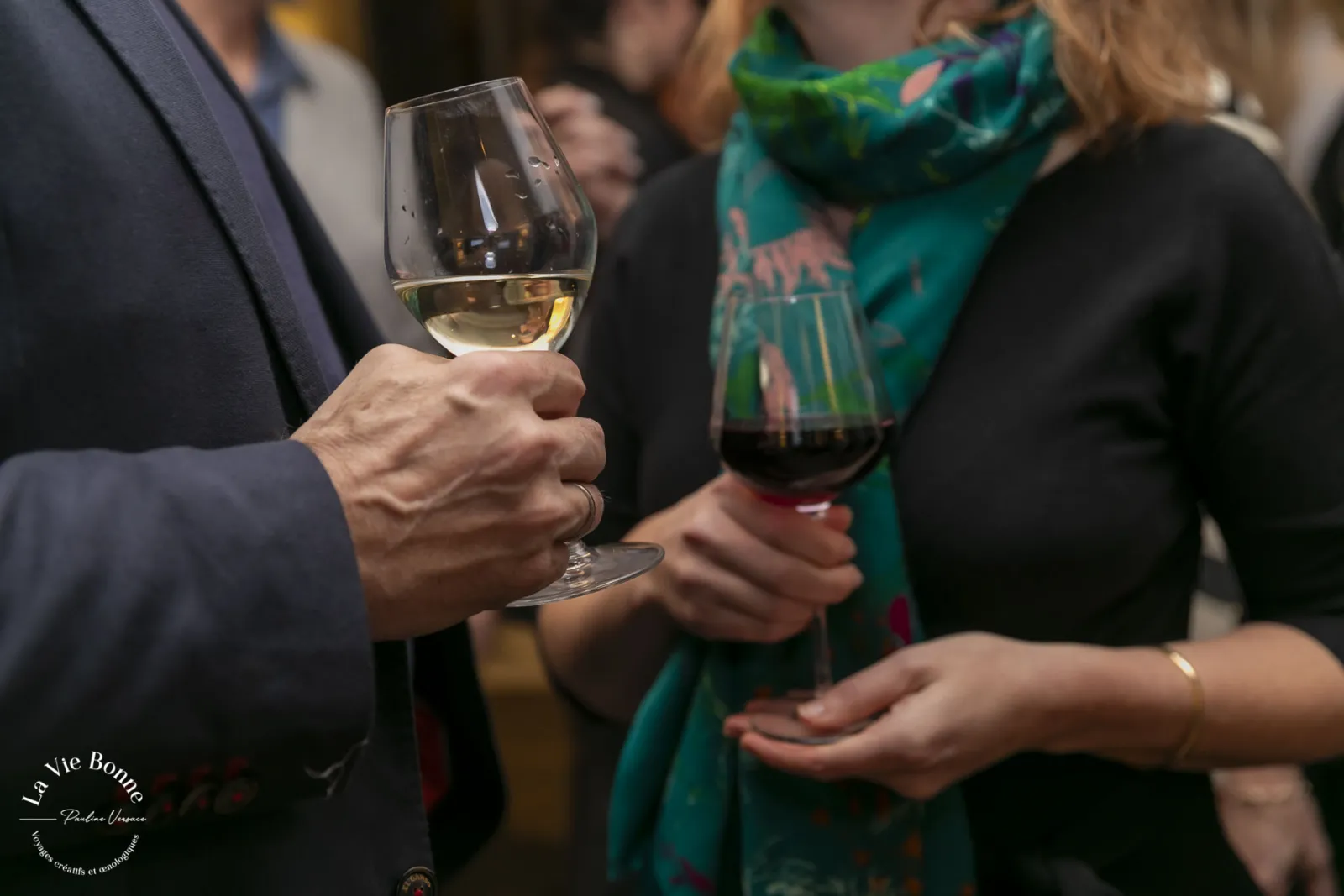 People enjoying wine tasting at a social gathering in Bordeaux, with a man in a dark suit holding a glass of white wine in the foreground