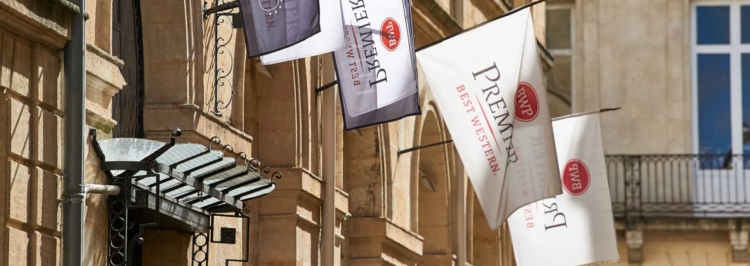 Exterior view of Best Western Premier Hotel Bayonne Etche Ona in Bordeaux, showing hanging banners on a historic stone building facade with ornate architectural details.