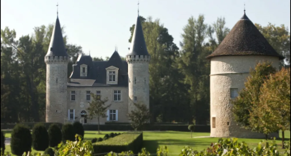 Château d'Agassac in Bordeaux, France, featuring a white stone castle with two tall towers with black pointed roofs, a central mansard roof, and a separate round tower on the right, surrounded by manicured gardens and trees.