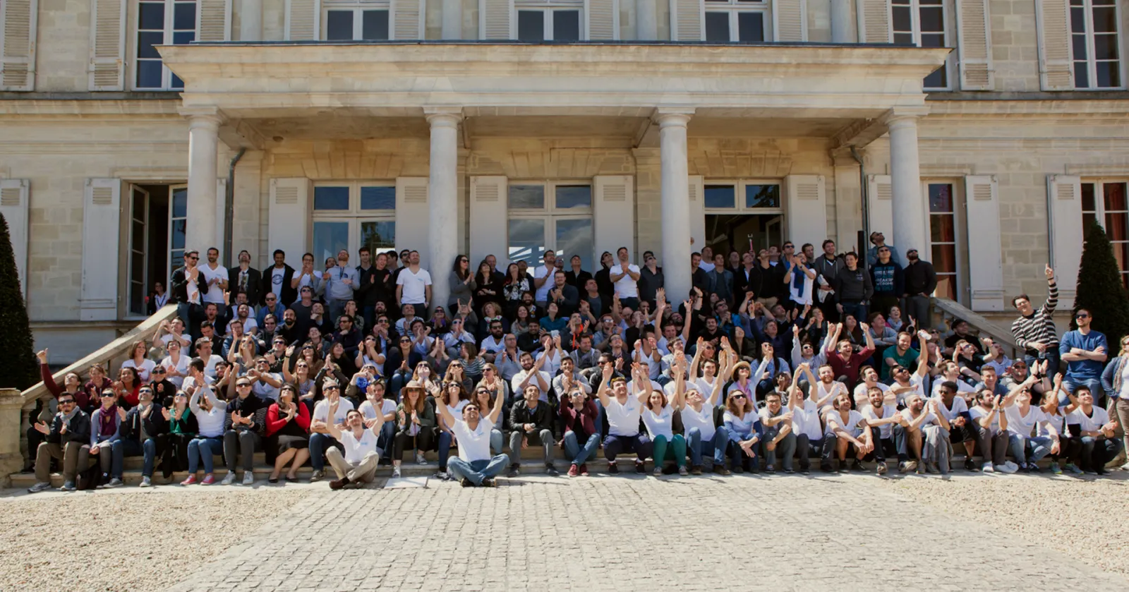 Large group photo of approximately 200 people gathered on the steps and courtyard of an elegant neoclassical building with white columns in Bordeaux, France.