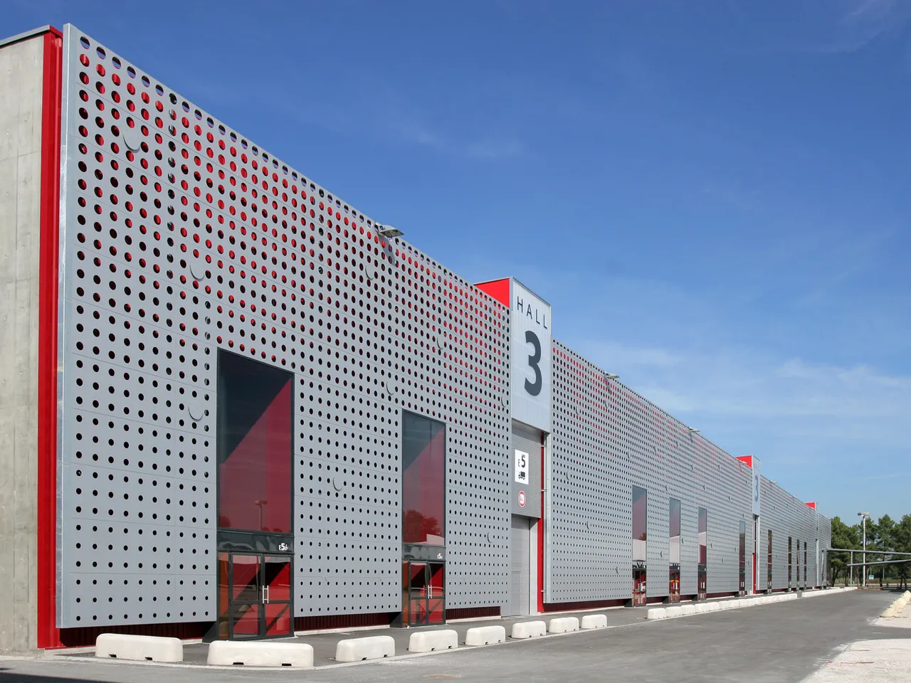 Modern exhibition hall with white perforated metal facade, red accents, and entrance marked 'Hall 3' at Bordeaux Exhibition Centre under clear blue sky
