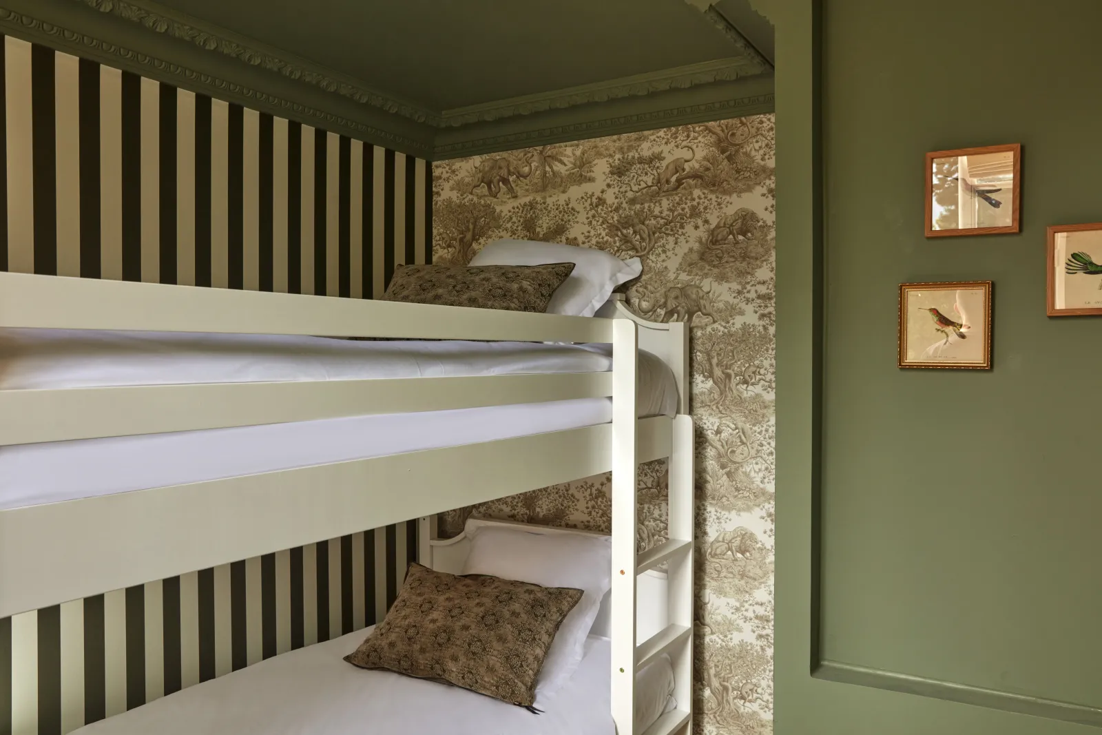 Bunk bed with white frame and striped headboard in a bedroom with green walls, toile wallpaper, and framed bird prints at Château Léognan in Bordeaux.