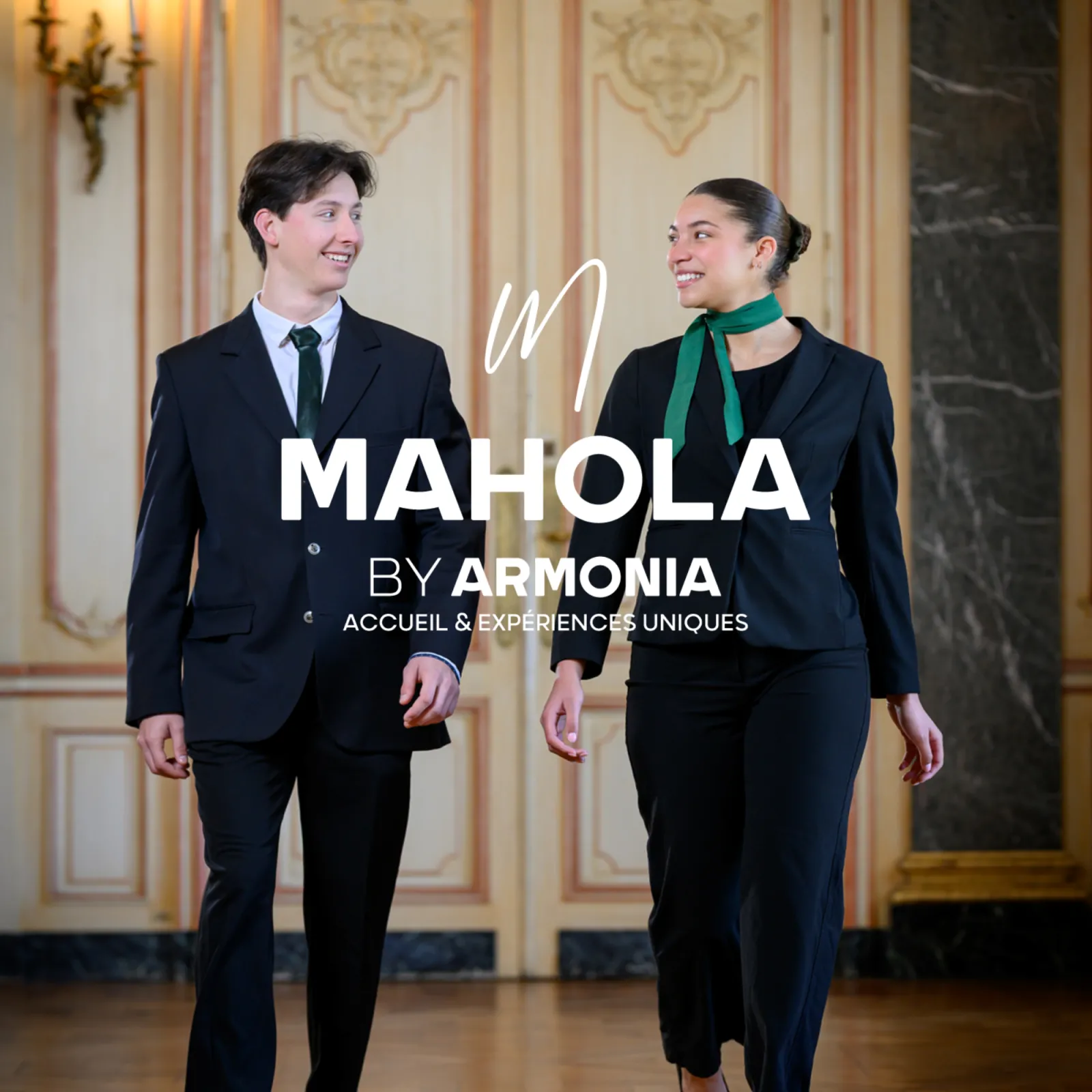 Two professionally dressed staff members walking through an elegant classical corridor with ornate cream and gold paneling, promoting Mahola by Armonia hospitality services in Bordeaux.