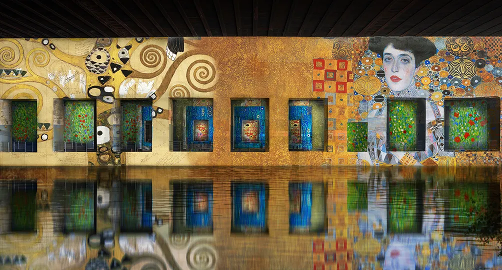 Ornate building facade with golden and blue tones reflected in water, featuring decorative spirals, geometric patterns, and a portrait of a woman, located at the Bassins des Lumières in Bordeaux.