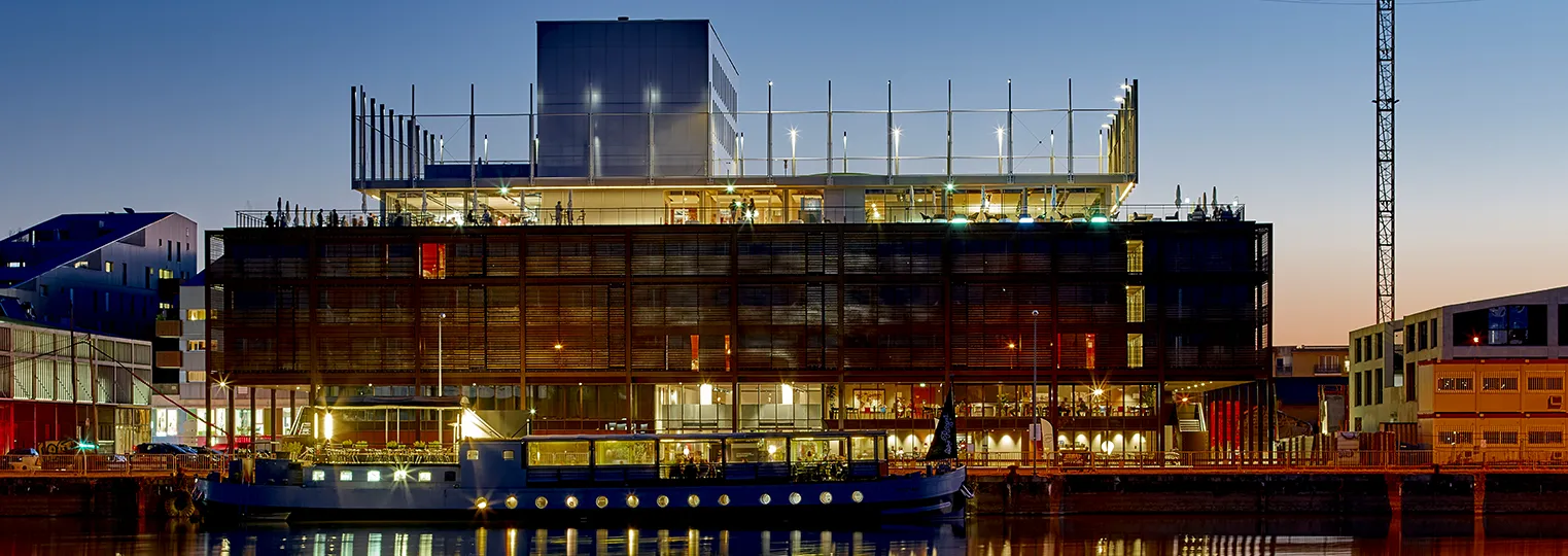 Modern Radisson Blu Hotel building in Bordeaux with illuminated glass and metal facade reflected in water at dusk, featuring contemporary architecture with distinctive lighting.