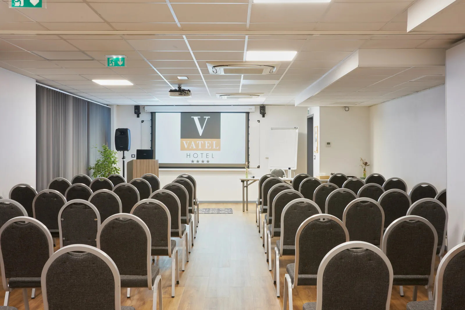 Conference room at Vatel Hotel in Bordeaux with rows of black upholstered chairs facing a projection screen displaying the Vatel Hotel logo