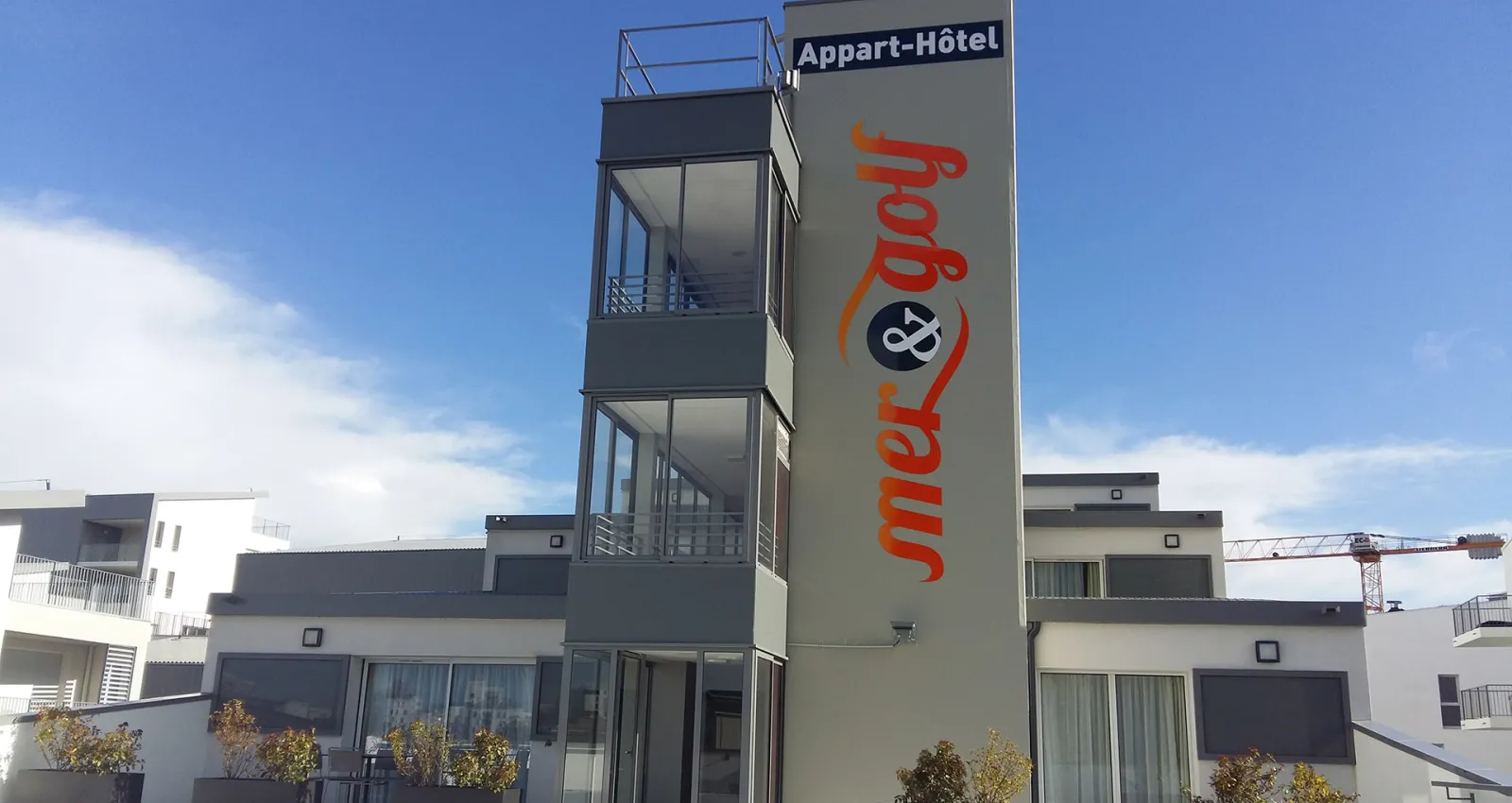Modern aparthotel building with 'mer&golf' branding, featuring a tall glass elevator shaft and contemporary architecture in Bordeaux's Bassins à Flot district