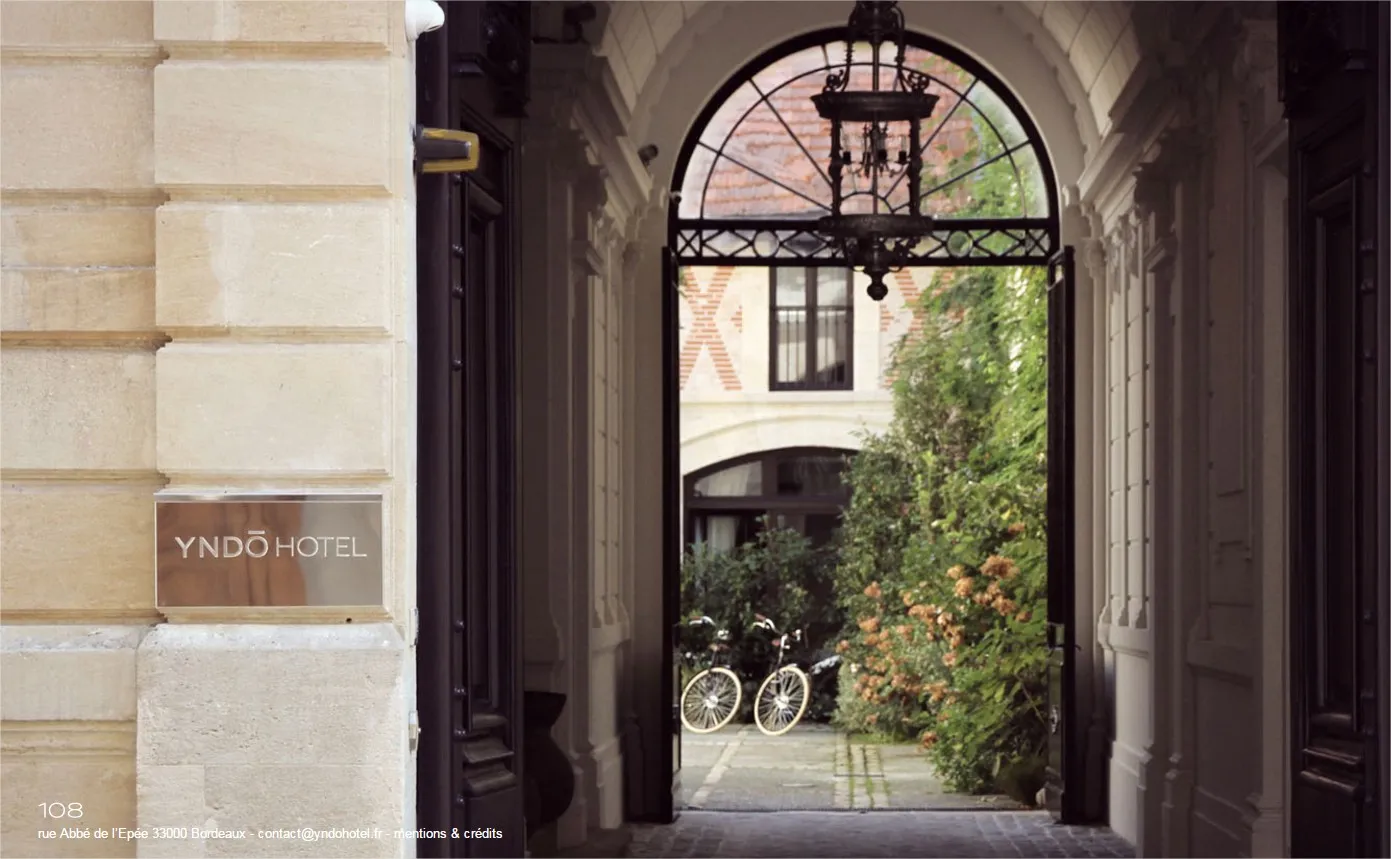 Entrance to Yndo Hotel in Bordeaux showing an elegant arched doorway with wrought iron details, leading to a courtyard with ivy-covered walls and bicycles