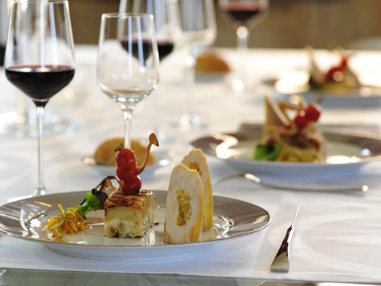 Fine dining plated dessert at Le Nectar Traiteur in Bordeaux, featuring a layered cake with red currant garnish, accompanied by wine glasses and elegant table setting