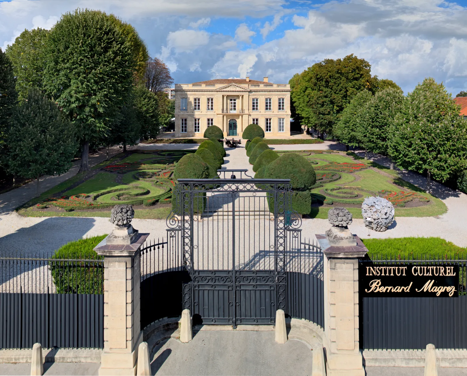 Grand entrance gate of the Bernard Magrez Cultural Institute in Bordeaux, with a neoclassical mansion visible beyond manicured gardens and topiary hedges.
