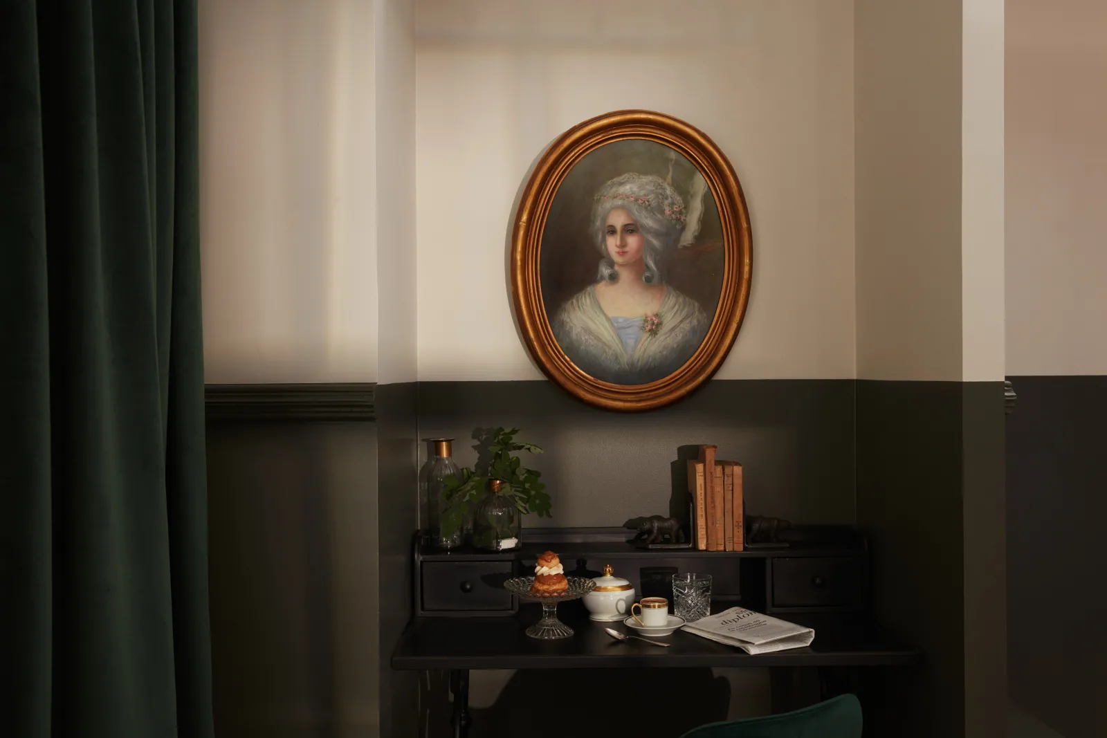 An elegant interior at Château Léognan in Bordeaux featuring a classical portrait of a woman in a golden oval frame hanging above a dark desk with books, decorative objects, and tea service.