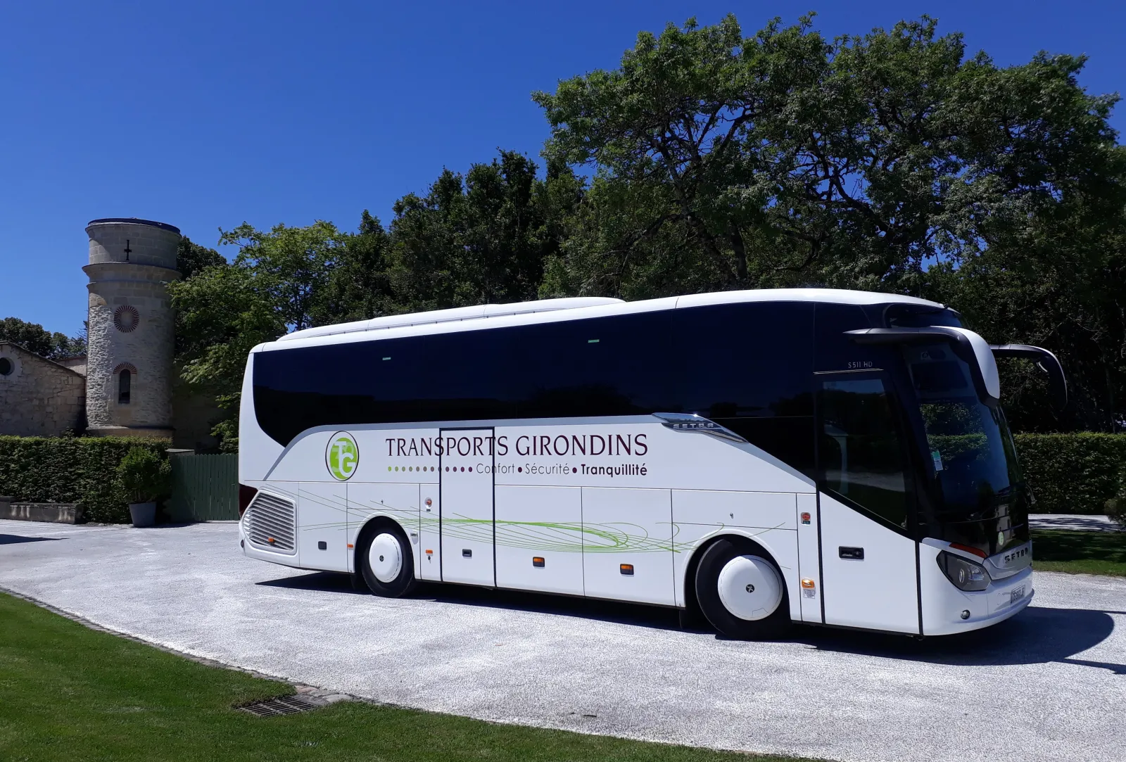 White coach bus from Transports Girondins parked in front of a stone tower and trees in Bordeaux