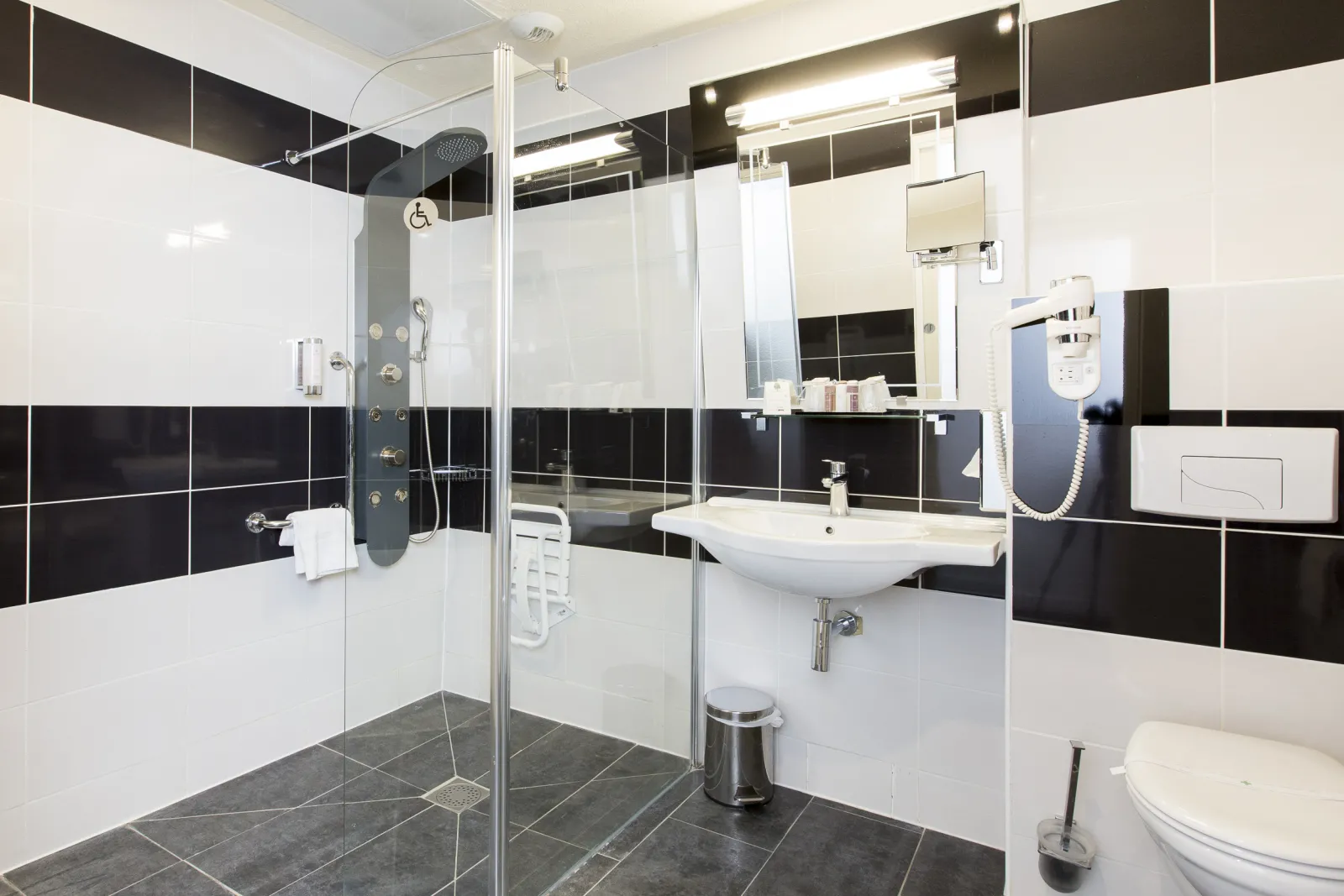 Modern bathroom at Quality Hôtel Bordeaux Centre featuring a spacious walk-in shower with glass enclosure, white and black tile design, vessel sink, mirror, and accessible facilities