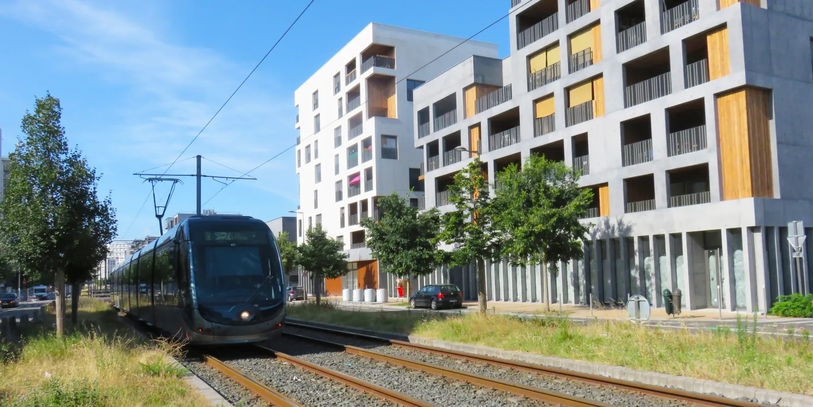 Modern tram traveling on tracks in front of contemporary white apartment buildings with yellow balconies in an urban neighborhood