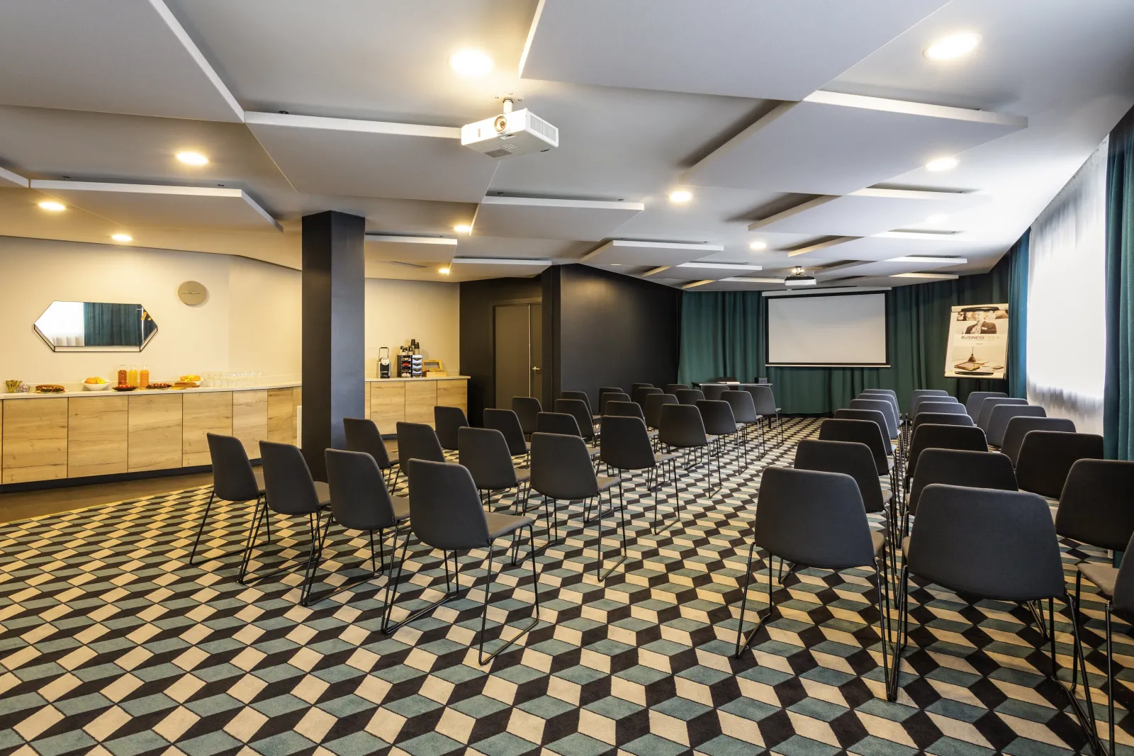 Modern conference room at Mercure Bordeaux Centre hotel with rows of black chairs facing a projection screen, geometric patterned flooring, wooden reception counter, and contemporary ceiling design with recessed lighting