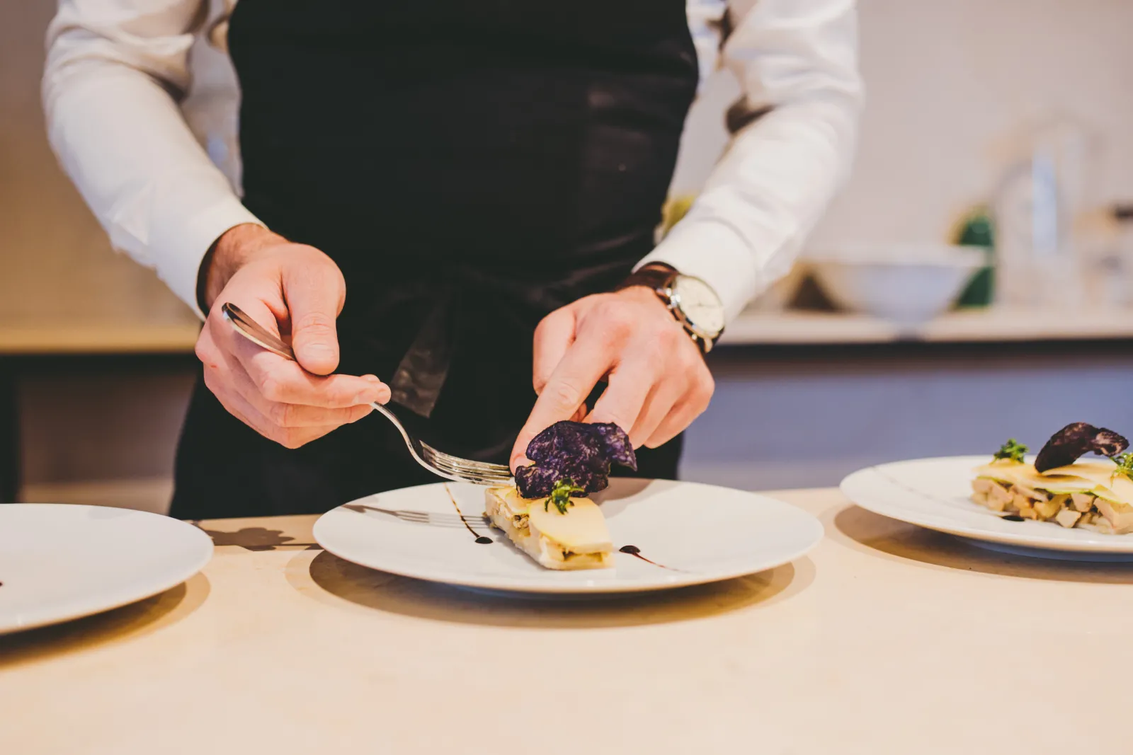 Chef plating a gourmet dish with purple beetroot and garnish on a white plate in an upscale restaurant kitchen