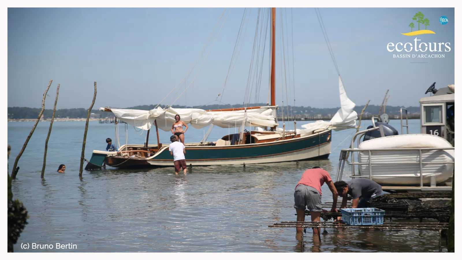 Traditional sailboat moored in shallow water with people wading and working on the shore in Arcachon Bay, a scenic maritime landscape with wooden pilings and coastal buildings.