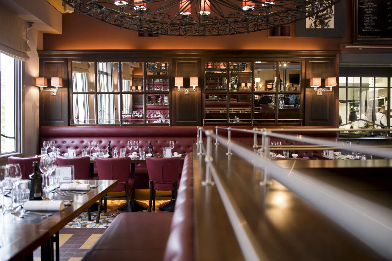 Elegant fine dining restaurant interior featuring burgundy leather banquettes, wooden paneling, ornate ceiling details, and display cabinets with ambient lighting at Como Cordeillan-Bages in Bordeaux.
