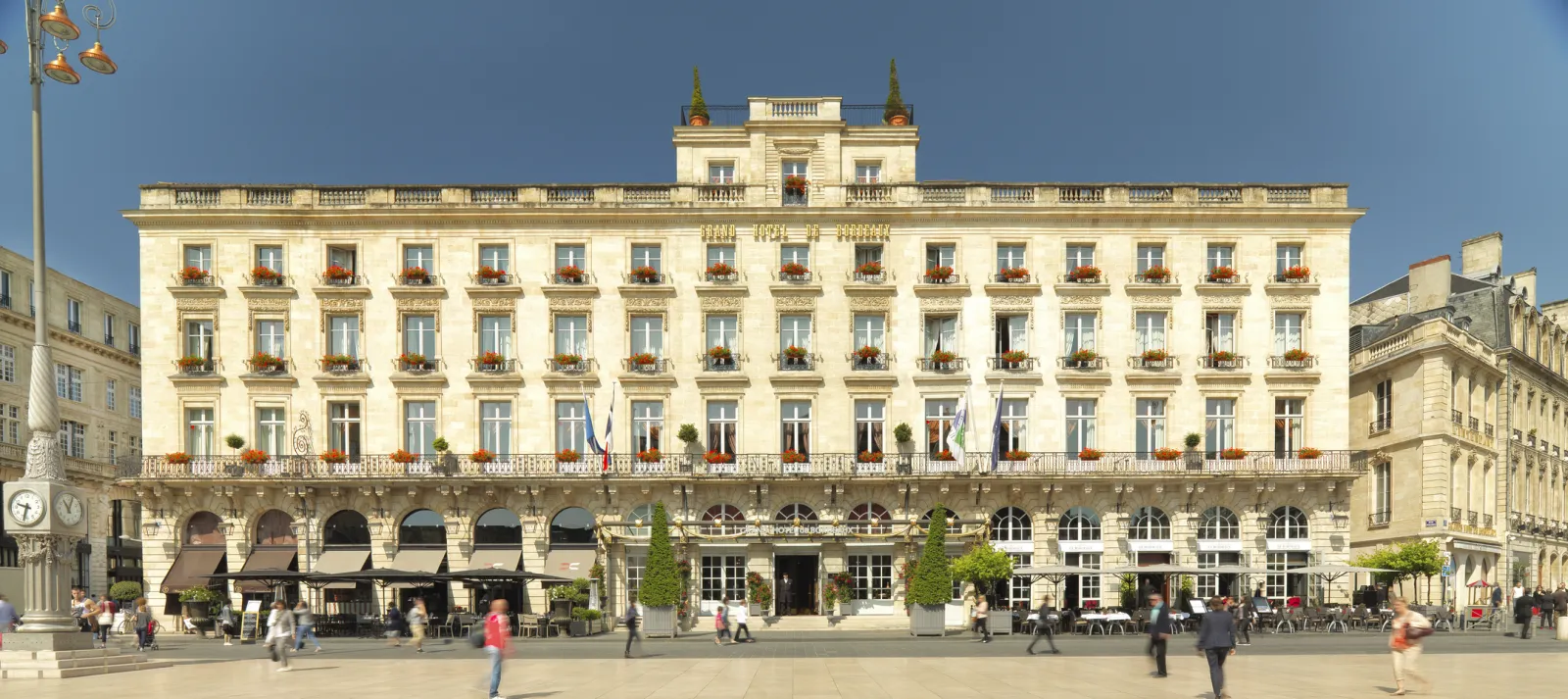 The Intercontinental Grand Hôtel de Bordeaux, an elegant 18th-century neoclassical building with cream-colored stone facade, ornate balconies, and mansard roofs with golden spires, facing a public plaza in downtown Bordeaux.
