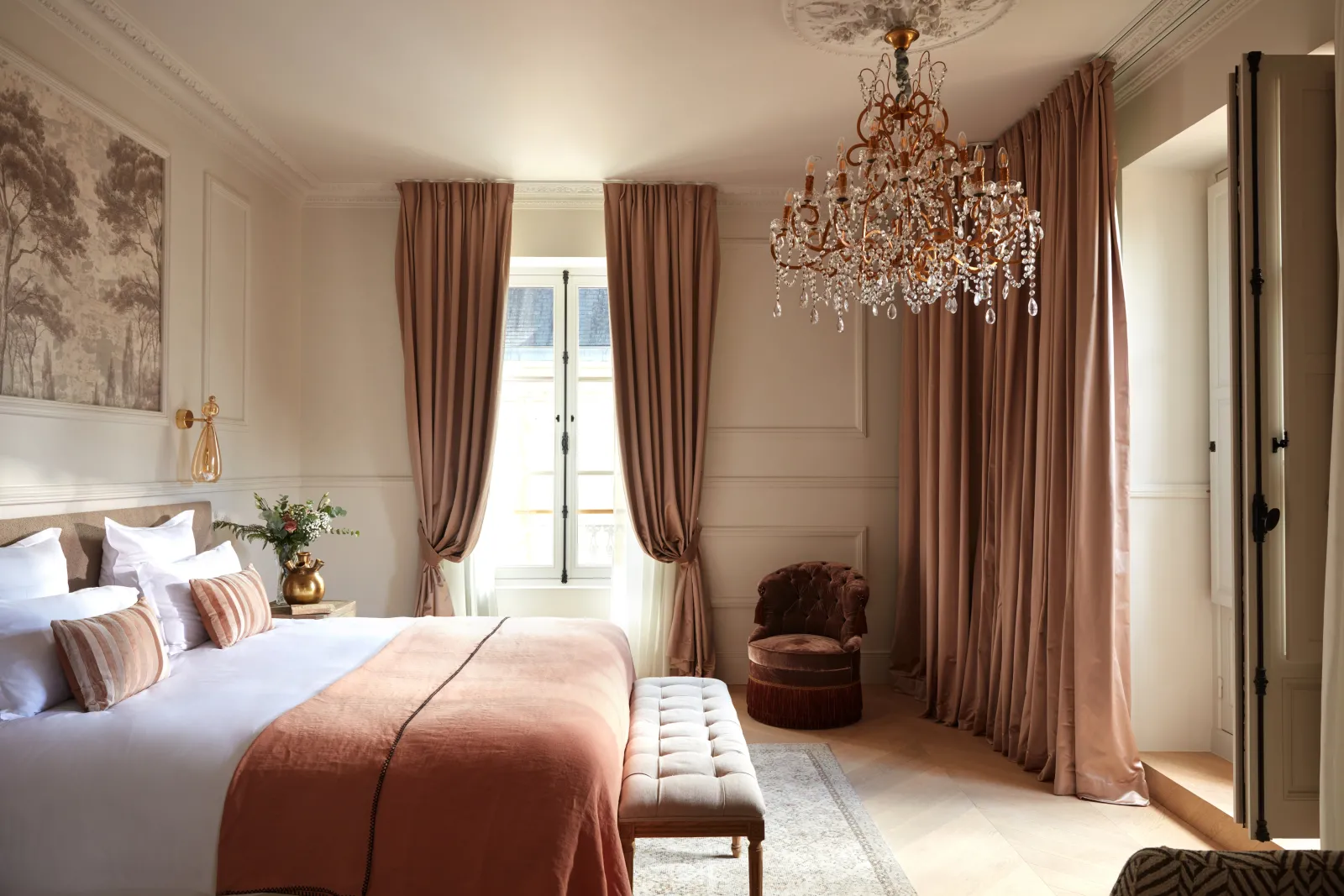 Luxurious bedroom with a king-size bed, crystal chandelier, rose-toned curtains, and elegant furnishings at Château Léognan in Bordeaux