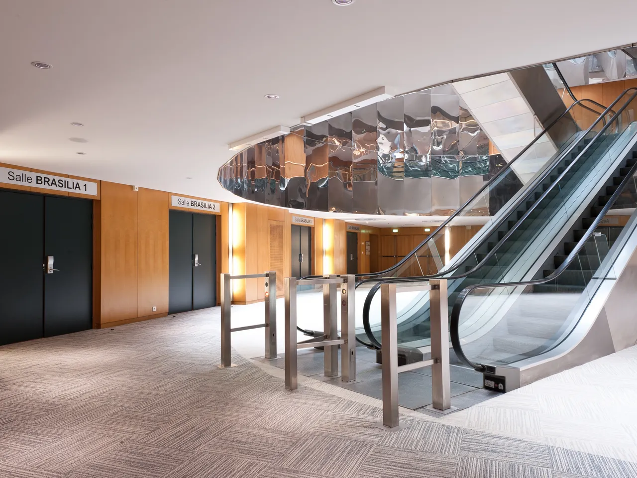 Modern interior of Cité Mondiale Convention Centre in Bordeaux featuring escalators, wooden-paneled meeting rooms labeled Salle Brasilia 1 and 2, contemporary lighting, and polished geometric flooring.