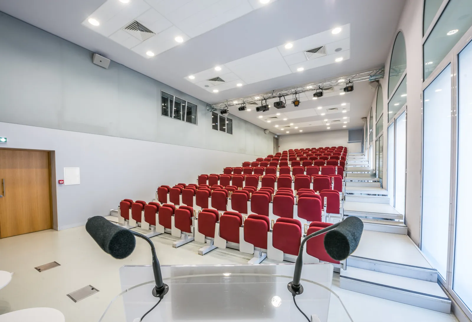 Modern auditorium with red seats arranged in rows, professional microphones in the foreground, white walls, recessed lighting, and glass partition on the right side at Bordeaux Palais de la Bourse.