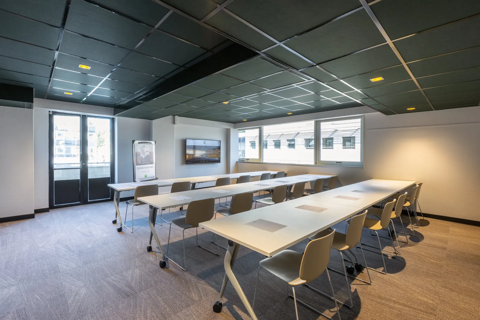Modern conference room at Ibis Styles Bordeaux Meriadeck with mobile tables, ergonomic chairs, suspended ceiling with integrated lighting, large windows, and audiovisual equipment.
