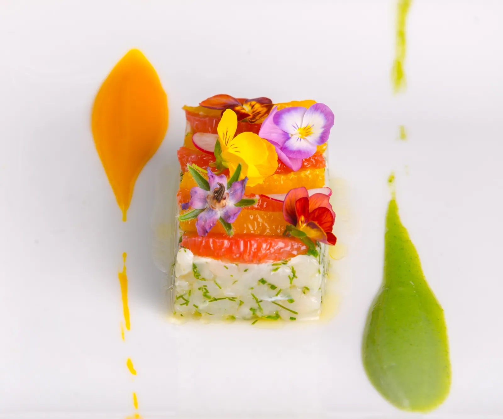 Gourmet layered dish from Maison Dulou Traiteur in Bordeaux, featuring fresh vegetables, edible flowers, and decorative sauce dots on a white plate