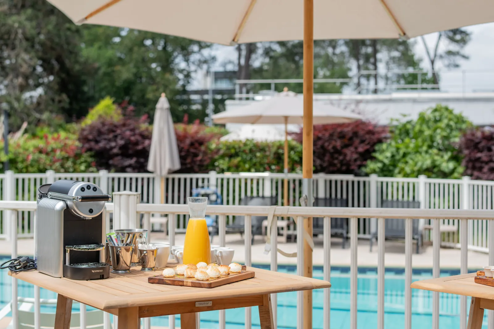 Outdoor poolside breakfast setup at Novotel Bordeaux Mérignac with coffee machine, fresh pastries, orange juice, and shaded seating overlooking the swimming pool
