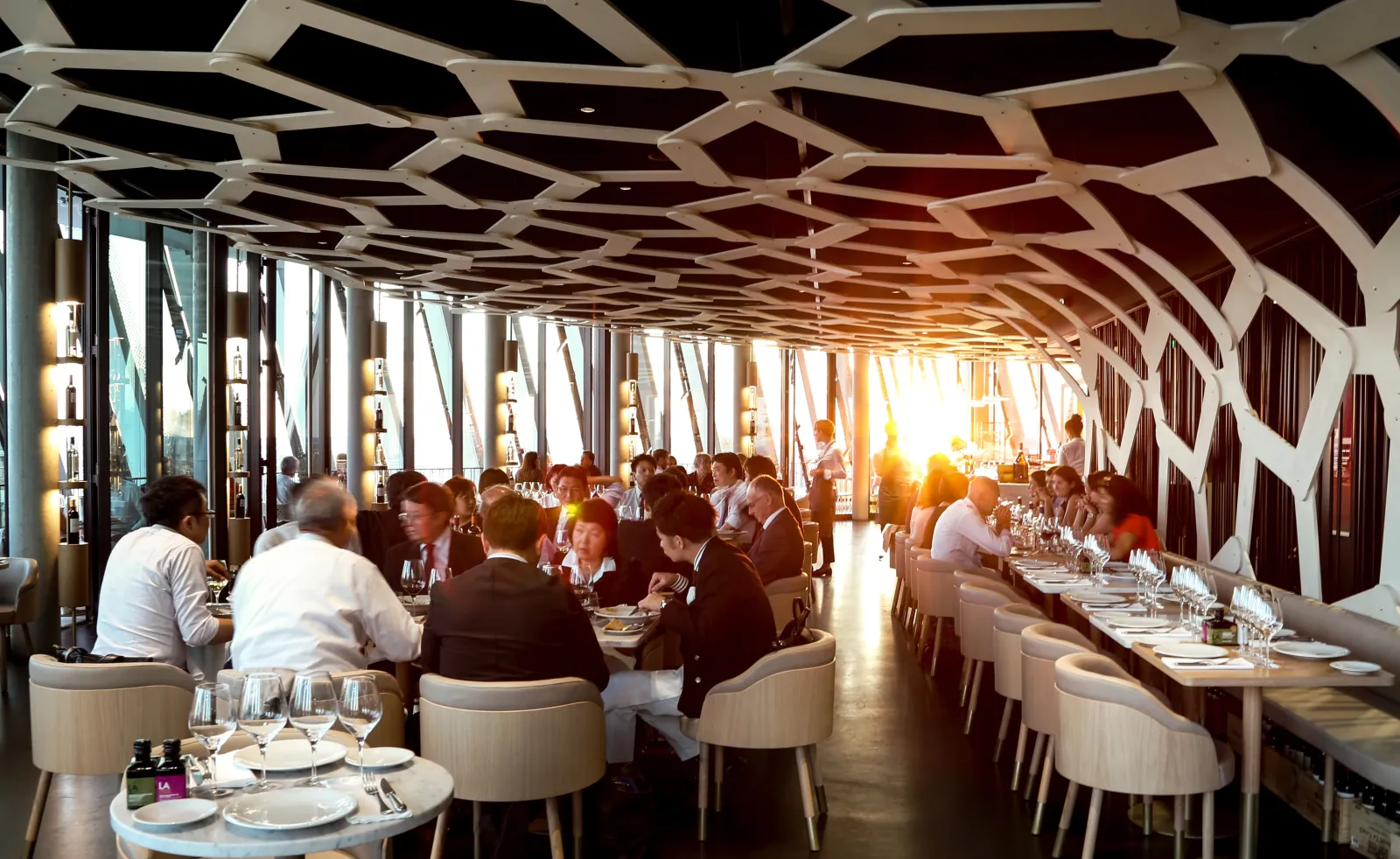 Panoramic restaurant interior at La Cité du Vin in Bordeaux, featuring modern geometric ceiling design, floor-to-ceiling windows overlooking the city, and diners seated at tables during an event.