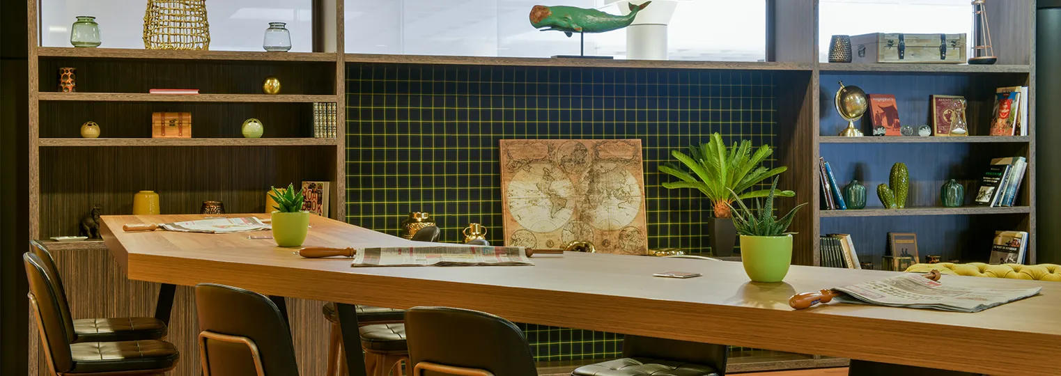 Modern office workspace with wooden desk, green potted plants, vintage world map, shelving units with books and decorative items, dark tiled accent wall, and leather chairs at the Mercure Bordeaux Château Chartrons hotel.