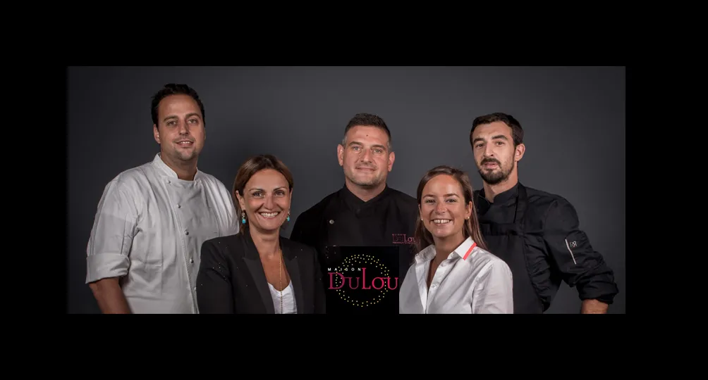 Five smiling team members from Maison Dulou Traiteur posing together against a gray background, with the company logo visible on one person's shirt