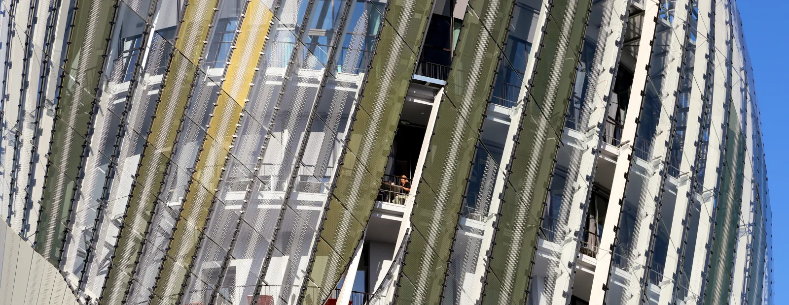 Modern residential building facade with vertical green and white mesh screens and balconies under clear blue sky in Bordeaux