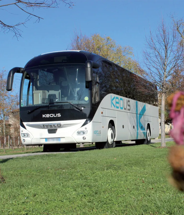 White and black Iveco coach bus with Keolis branding parked on a grass area with autumn trees in the background in Bordeaux