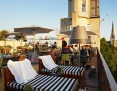 Rooftop terrace of Mama Shelter Bordeaux with striped loungers, umbrellas, and city views including the cathedral tower