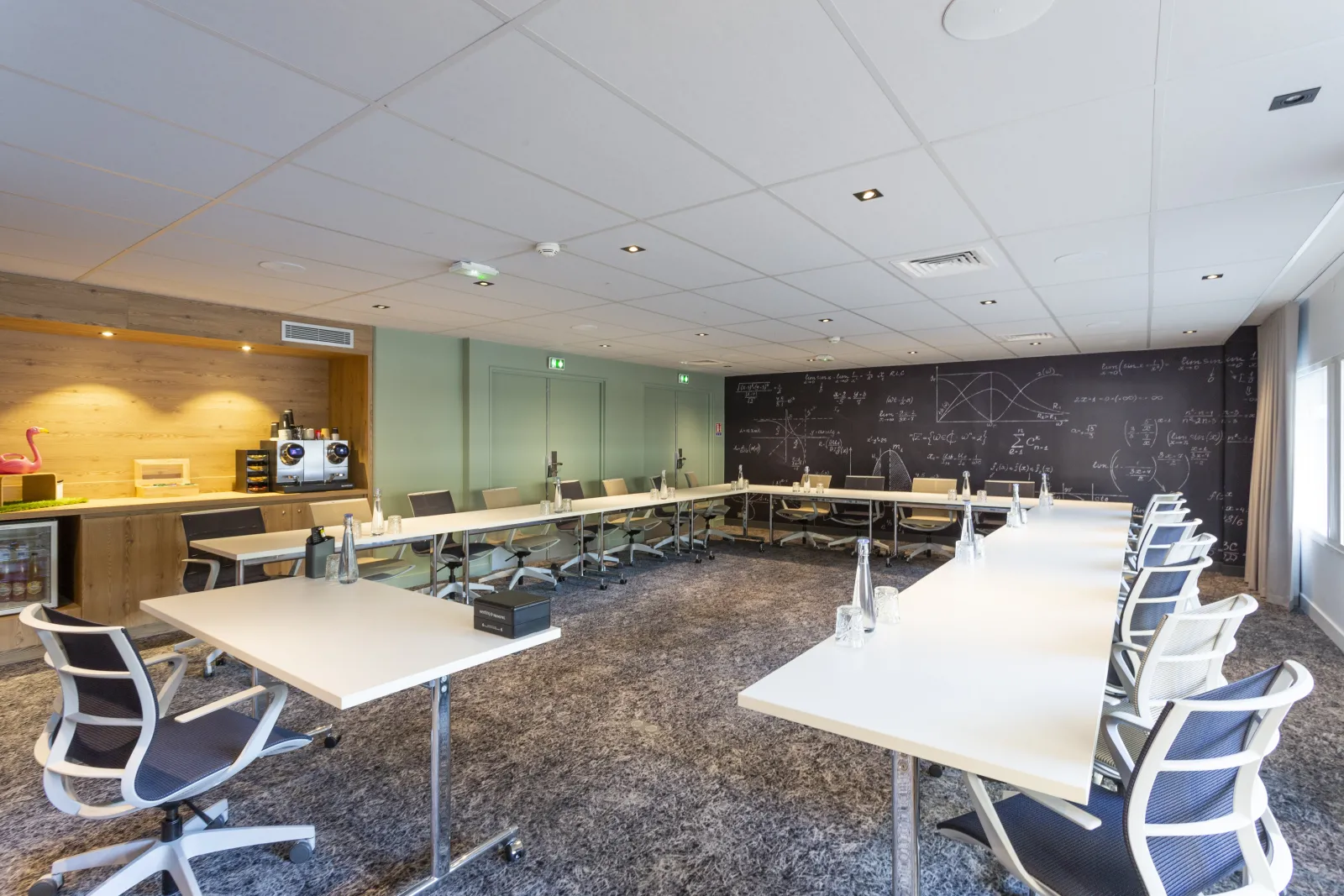 Modern conference room at Novotel Bordeaux Centre featuring multiple white tables with blue ergonomic chairs, a blackboard wall with mathematical equations, yellow accent lighting, and green glass partitions