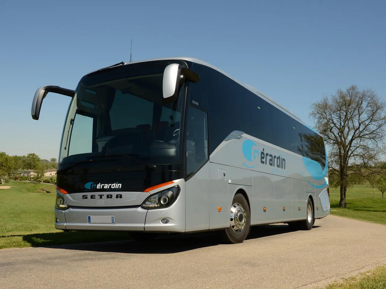White and dark blue Setra coach bus with Gérardin branding parked on a country road near Bordeaux, with green meadows and trees in the background.