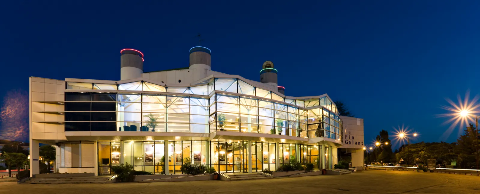 Modern glass and steel building illuminated at night with three cylindrical towers on the roof, located in Bordeaux's Pin Galant district